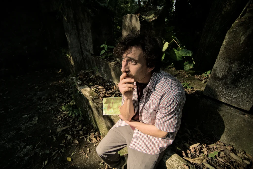 A man sits looking lost in the ruins of an old building in the jungle.
